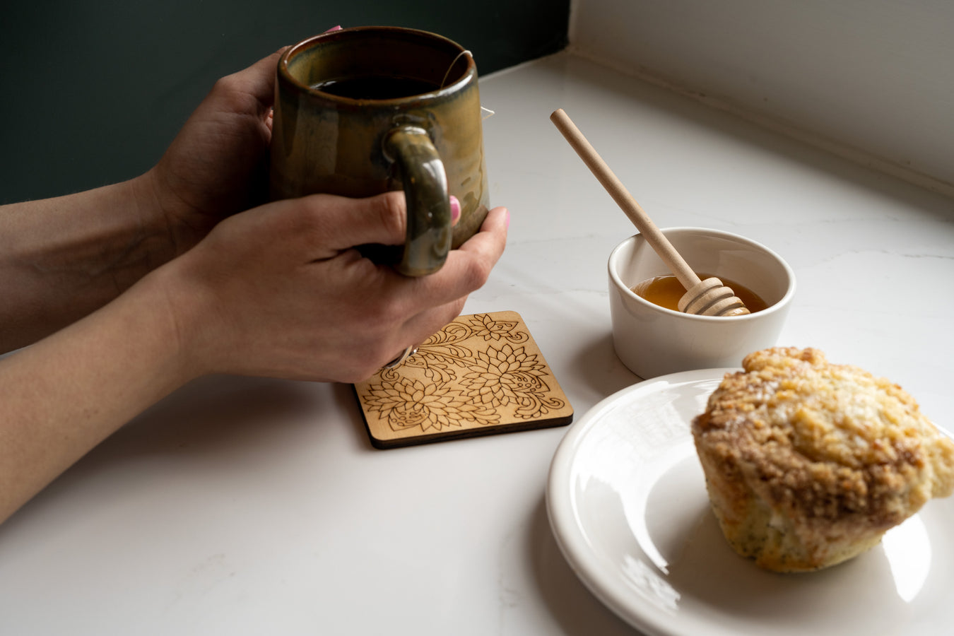 Our tablescape collection features coasters, trivets, napkins, and limited edition wooden floral stems. Make your table setting beautiful with these unique products. Shown here is a wooden coaster styled with a ceramic mug, muffin and honey.