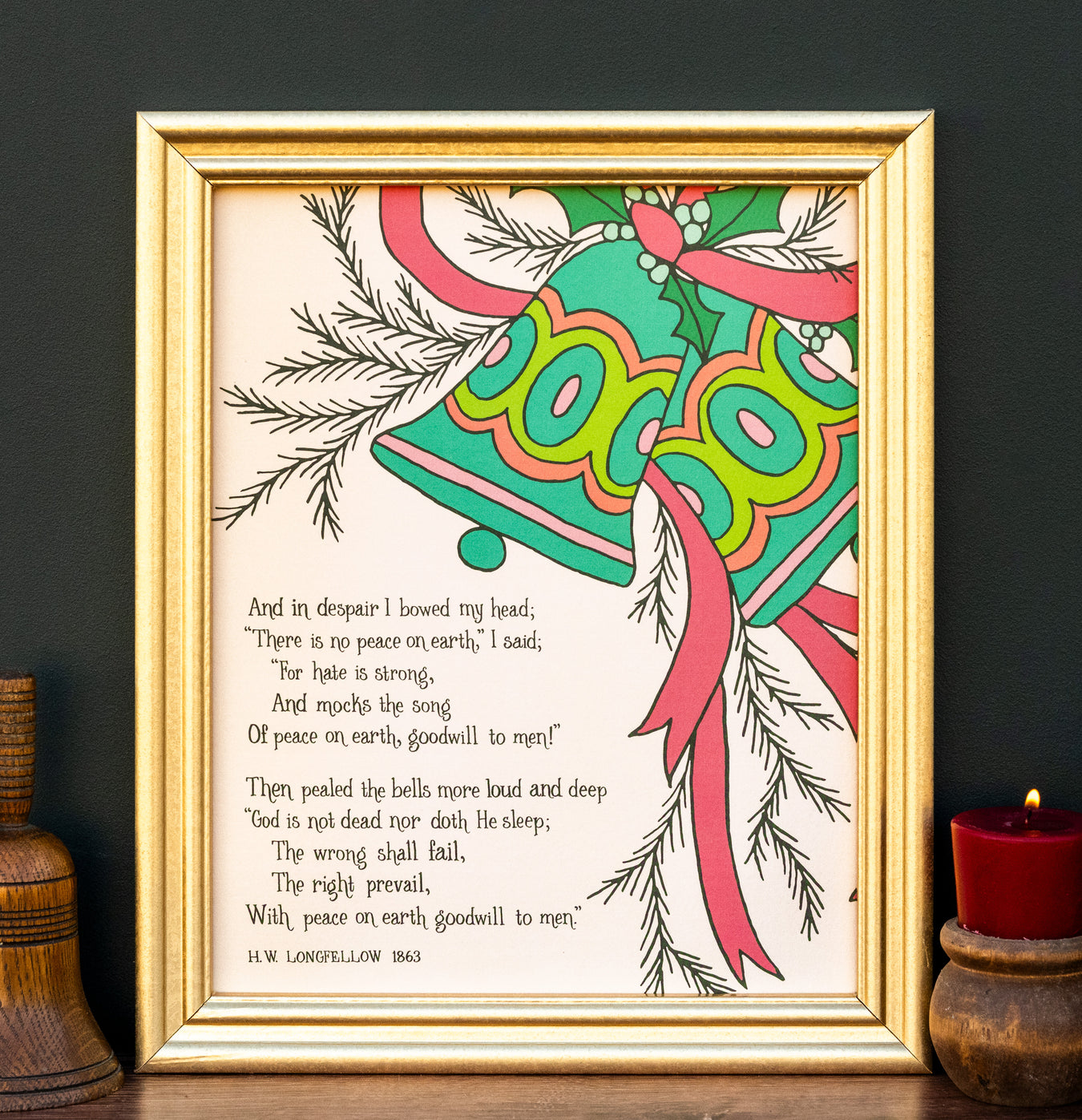 The "I Heard the Bells on Christmas Day" hymn art print features a verse from the beloved seasonal hymn, surrounded by greenery and bell illustrations against a creamy vanilla background—shown in a gold frame and styled with a wooden bell and a candle.