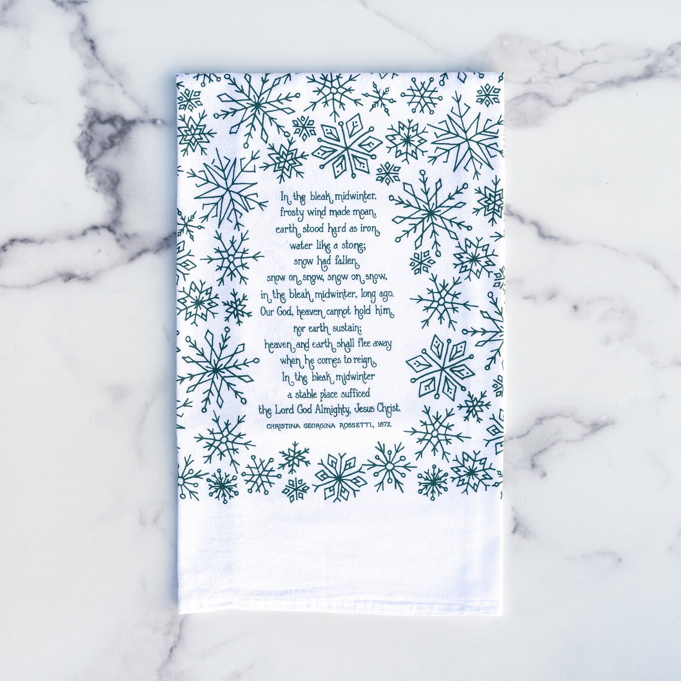 In the Bleak Midwinter Christmas hymn tea towel is hand-lettered with a festive snowflake border and printed in evergreen on a 100% cotton tea towel, shown folded on a marble background.