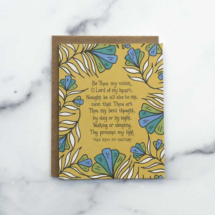 The Be Thou My Vision hymn greeting card, framed by rainforest green and stormy blue colored florals against a saffron background, shown with a kraft paper envelope against a marble background.