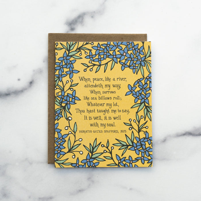 The It Is Well With My Soul hymn greeting card, framed by stormy blue and lime sorbet colored florals against a buttercream background, shown with a kraft paper envelope against a marble background.