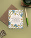 The For the Beauty of the Earth hymn greeting card, framed by asparagus and blue lagoon floral against a moonstone background, is styled with a kraft paper envelope, two-toned ink pen, and a mug with coaster.