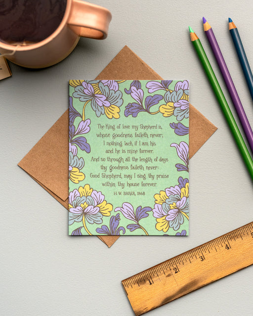 The King of Love My Shepherd Is hymn greeting card, framed by lavender gray and vintage yellow floral against a dark mint background, styled with a kraft paper envelope, colored pencils, a ruler, and a mug.