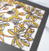 Detail image of the Layered Floral Papercut “Audrey” (Light Gray) which is made using cardstock in hues of dark gray, orange fizz, mustard, and light gray.