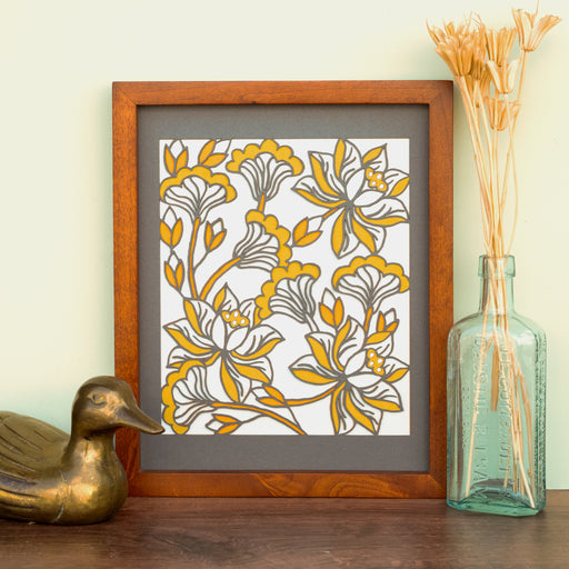 The Layered Floral Papercut “Audrey” (Light Gray) is made using cardstock in hues of dark gray, orange fizz, mustard, and light gray, shown framed and styled with a glass vase holding dried grasses and a bronze duck figurine.