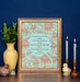 Hymn art print of Christ the Lord is Risen today, featuring hand-lettered hymn text and hand illustrated florals in corals and pinks against a mint green background, displayed in a gold frame and styled with vase of fresh greens, candles, and ceramic figurines against a navy wall.