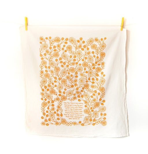 Come Thou Fount hymn tea towel is printed in butterscotch and features hand lettered hymn text surrounded by illustrated florals, pictured unfolded and hanging with clothes pins.