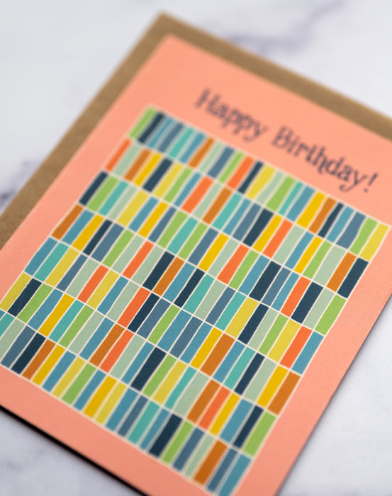 Happy Birthday greeting card with a peach background and a multi-colored grid pattern showing detail