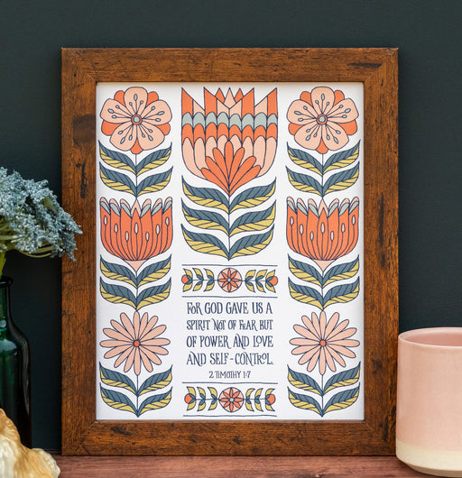 The "For God Gave Us" Scripture art print features the hand-lettered verse accented by peach and coral flowers with a buttermilk background, shown in a wooden frame and styled with a vase of dried flowers and a mug.