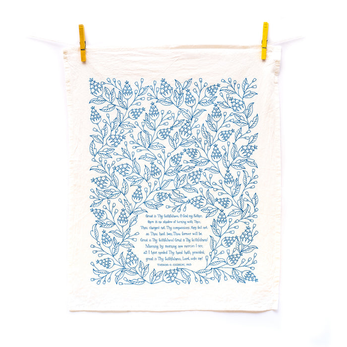 Great Is Thy Faithfulness tea towel is printed in a striking cerulean blue. The hand lettered text is surrounded by illustrated floral design, and the towel is shown unfolded and hanging at full length with clothes pins against a white background