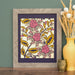 The Layered Floral Papercut “Lyra” (Violet) is made using cardstock in hues of violet, deep pretty pink, mustard, and cream, shown here framed and styled with a vase of dried flowers and a brass figurine.