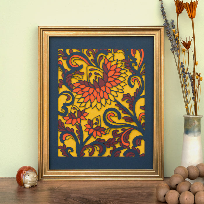 The Layered Floral Papercut “Margot” (Maroon) is made using cardstock in hues of flag blue, maroon, tangy orange, and mustard, shown framed and styled with a vase of dried flowers and wooden beads.