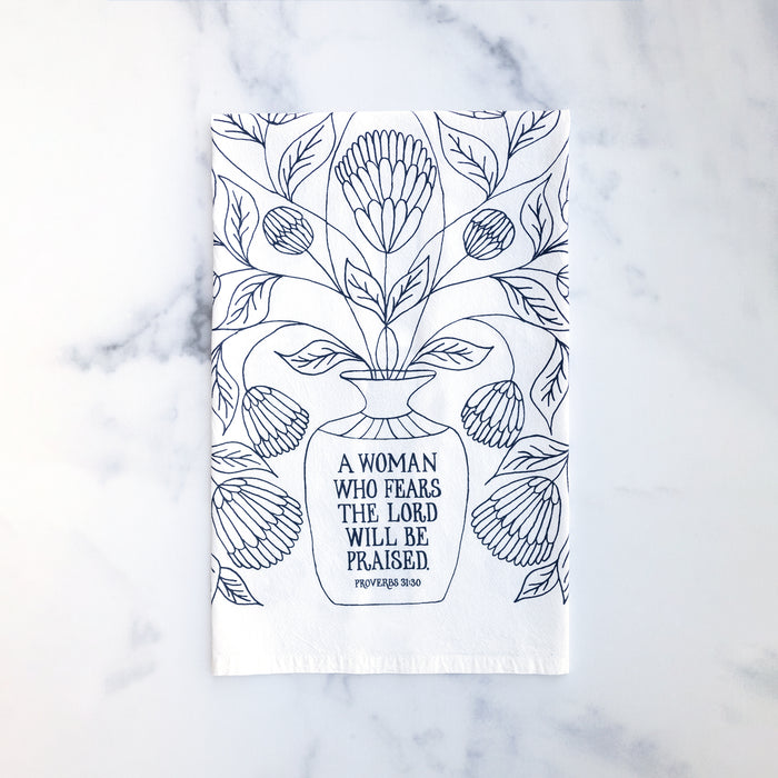 Bring wisdom and beauty into your home with The Woman Who Fears the Lord Scripture Tea Towel, featuring Proverbs 31 verses printed in midnight blue; 100% cotton. Shown folded against a marble background.