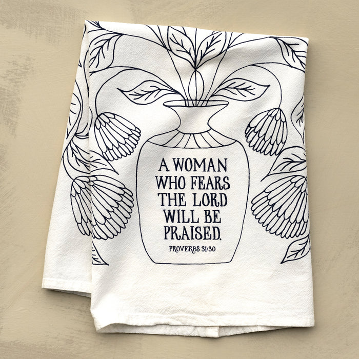 Bring wisdom and beauty into your home with The Woman Who Fears the Lord Scripture Tea Towel, featuring Proverbs 31 verses printed in midnight blue; 100% cotton. Shown folded against a khaki background.