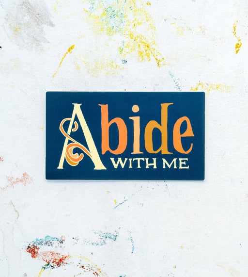 Introducing hymn stickers by Little Things Studio! The "Abide with Me" hymn sticker features multi-colored, hand lettered text with a botanical flourish, shown against a white worktable background.