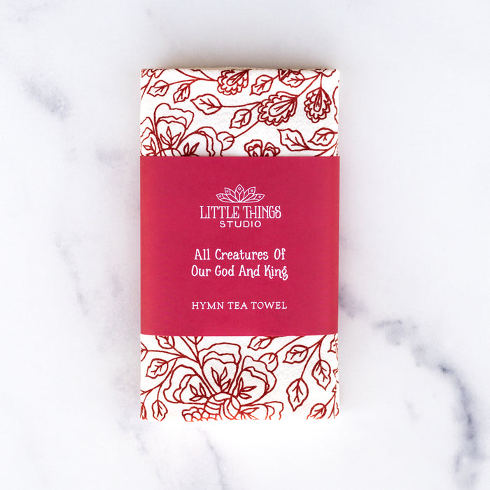 All Creatures of our God and King tea towel is printed in rich crimson, displayed folded with a paper belly band for gift giving