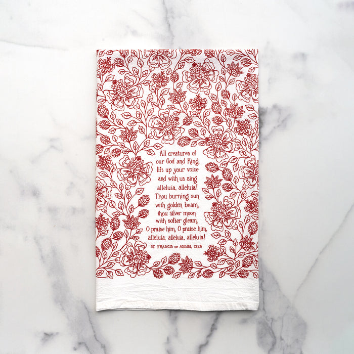 All Creatures of our God and King tea towel is printed in rich crimson, displayed folded against a white marble background