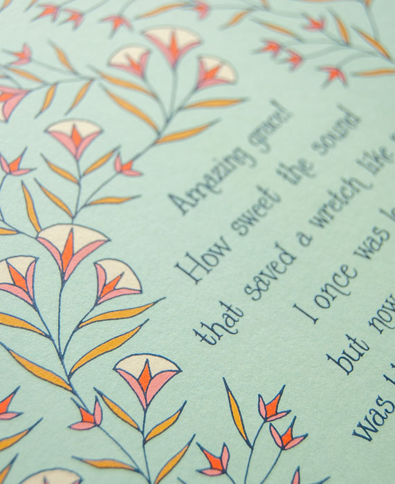 Hand lettered text detail of Amazing Grace art print on a sea foam green background surrounded by delicate illustrated florals in light red, yellow, and cream