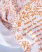 Floral and text detail of the Amazing Grace tea towel is one of our hymn tea towels, printed in pumpkin orange and featuring hand illustrated floral designs surrounding the hand lettered text