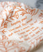 Floral and text detail of the Amazing Grace tea towel is one of our hymn tea towels, printed in marmalade orange and featuring hand illustrated floral designs surrounding the hand lettered text.