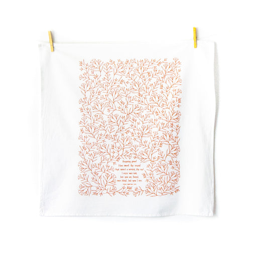 Amazing Grace tea towel is one of our hymn tea towels, printed in pumpkin orange and featuring hand illustrated floral designs surrounding the hand lettered text, shown folded and displayed unfolded and hanging with clothes pins