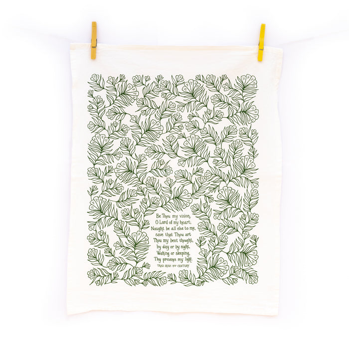 The Be Thou My Vision tea towel is printed in forest green and features hand lettered text surrounded by illustrated botanical detail, displayed unfolded and hanging with clothes pins.