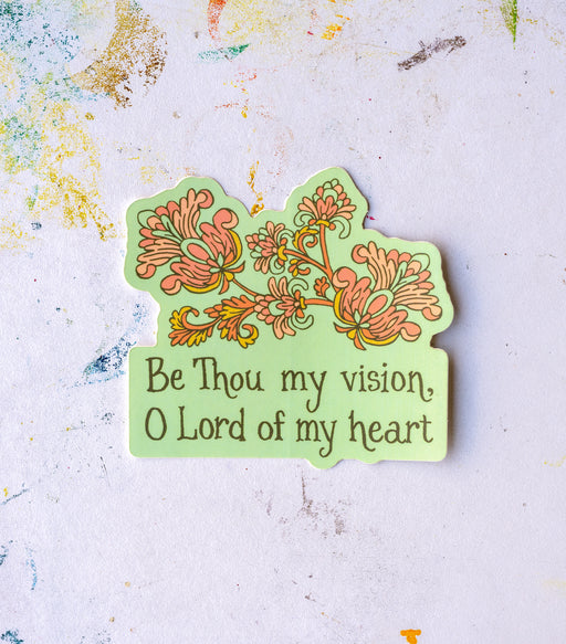 "Be Thou My Vision" hymn sticker has an aqua background with a coral and antique yellow motif. Shown against a paint-spattered worktable.