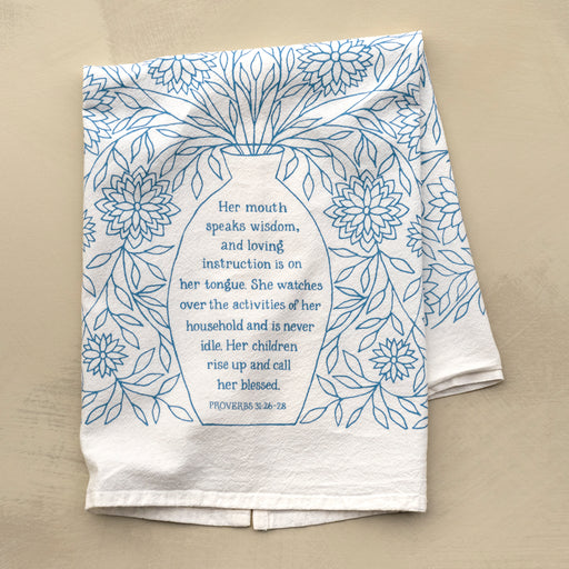 Bring wisdom and beauty into your home with the Call Her Blessed Scripture Tea Towel, featuring scripture verses printed in light blue; 100% cotton. Shown folded against a marble background.