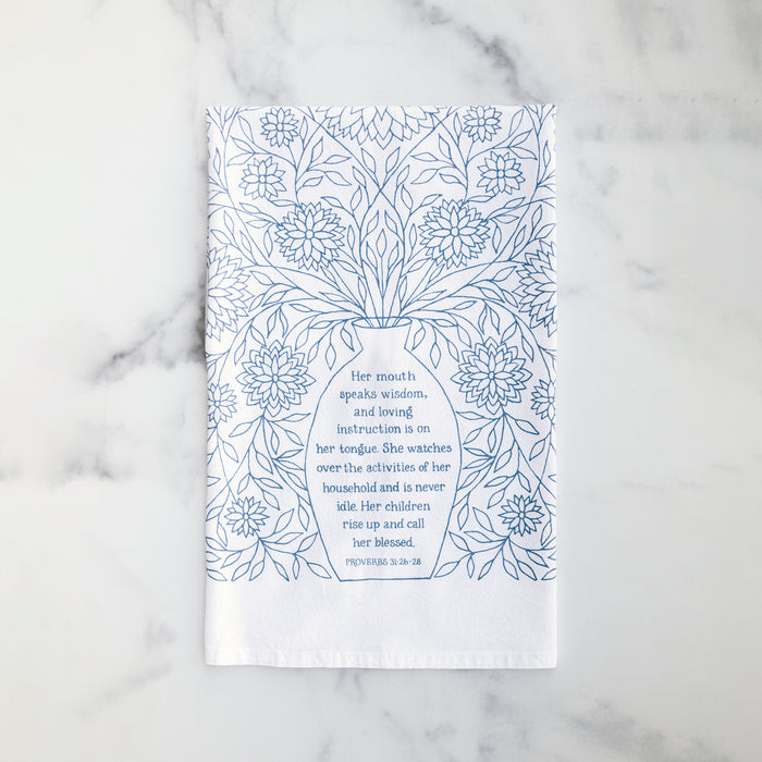 Bring wisdom and beauty into your home with the Call Her Blessed Proverbs Tea Towel, featuring scripture verses printed in light blue; 100% cotton. Shown folded against a marble background.