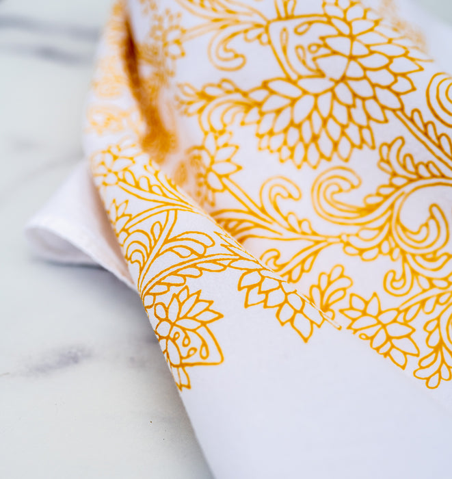 Little Things Studio presents floral tea towels featuring our unique illustrations in colorful hues. The Cordelia floral tea towel displays intricate florals in a cheerful daffodil, displayed here folded against a marble backdrop.