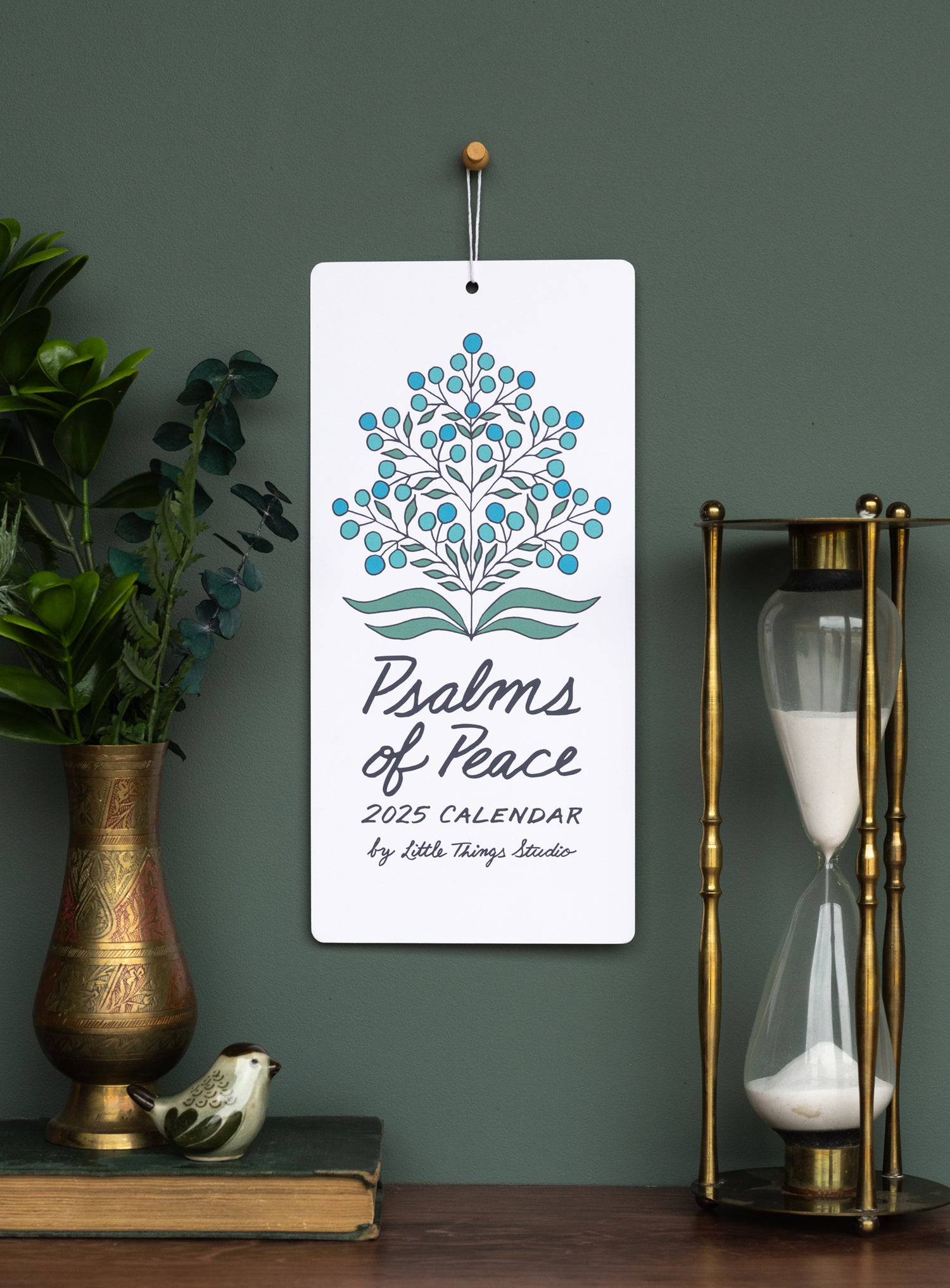 Celebrate 2025 with treasured verses from the Book of Psalms, accented by unique floral patterns and new script-style hand-lettering, shown here styled with greens in a bronze vase alongside an hour-glass.