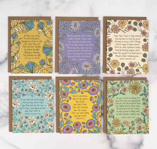 Each of the 6 hymn greeting cards in set "Crosby" features a hymn's lyrics on the front and its history on the back, shown here flat with recycled kraft paper envelopes against a marble background.