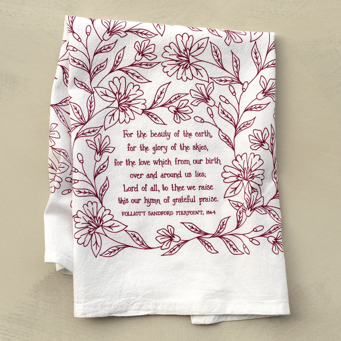 For the Beauty hymn tea towel is printed in pink plum and features delicate floral illustrations and hand-lettered lyrics from the hymn; shown folded against a khaki background.