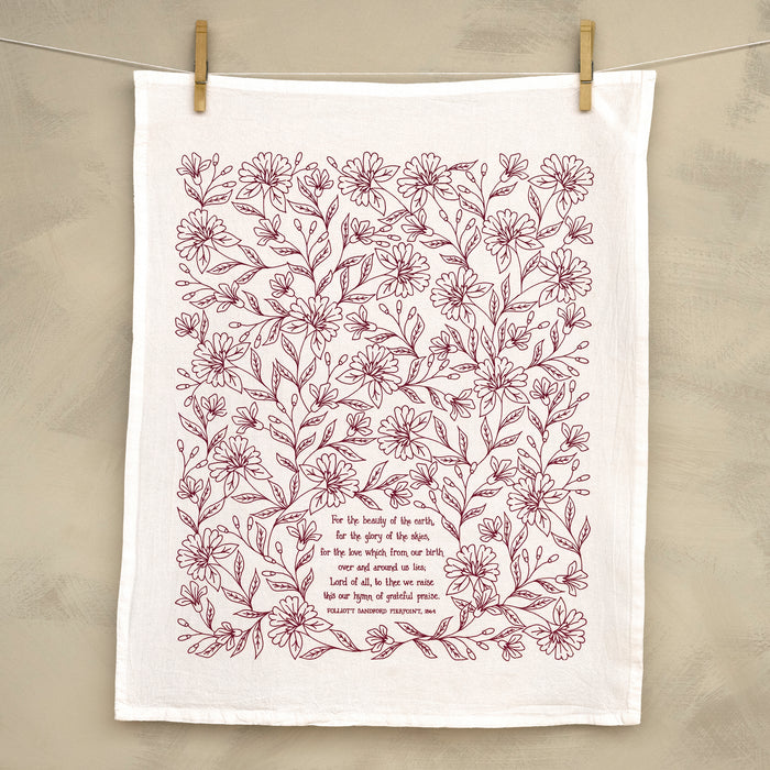 For the Beauty hymn tea towel is printed in pink plum and features delicate floral illustrations and hand-lettered lyrics from the hymn; shown unfolded and hanging with clothes pins