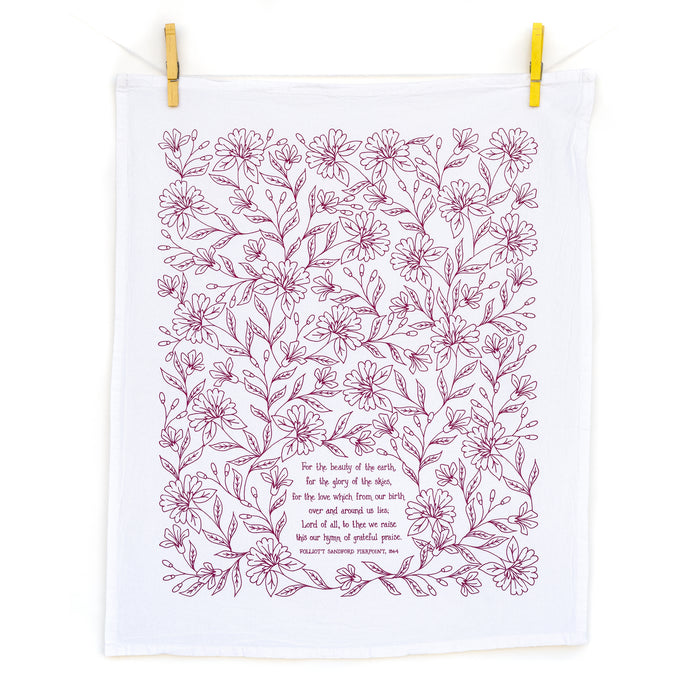 For the Beauty hymn tea towel is printed in pink plum and features delicate floral illustrations and hand-lettered lyrics from the hymn; shown unfolded and hanging with clothes pins