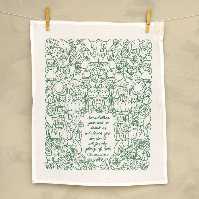 The For the Glory of God Scripture tea towel is printed in forest green and features 1 Corinthians 10:31, shown hanging with clothes pins