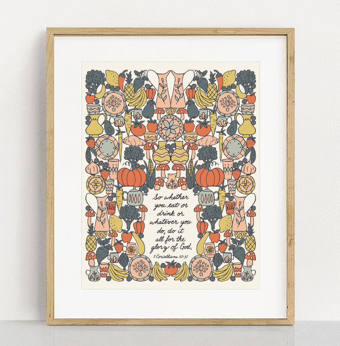 The "For the Glory of God" Scripture art print features a hand-lettered verse from I Corinthians accented by whimsical vegetable illustrations against a buttermilk background; shown in a gold frame against a white background.