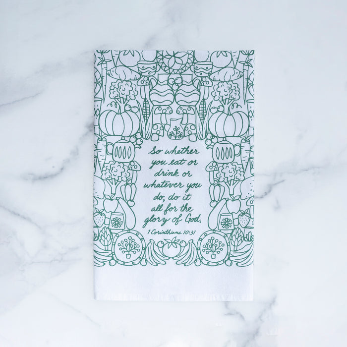 The For the Glory of God Scripture tea towel is printed in forest green and features 1 Corinthians 10:31, shown folded and set against a gray marble background.