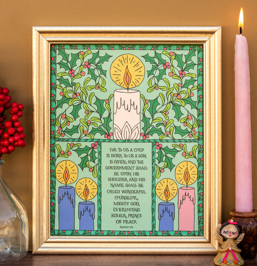 The For to Us a Child Is Born hymn art print features the beloved hymn text surrounded by illustrations of holly and advent candles against a wintergreen background; shown here in a gold frame and styled with red berries, a candle, and a ceramic figure.