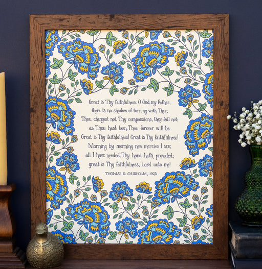 Great Is Thy Faithfulness hymn art print features the cherished hymn, surrounded by a bold blue and gold toned floral against a cream background; shown styled in a dark wood frame with a candle and a vase of flowers.