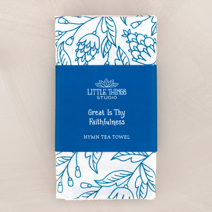 Great Is Thy Faithfulness tea towel is printed in a striking cerulean blue. The hand lettered text is surrounded by illustrated floral design, and the towel is shown folded and wrapped with a paper belly band.