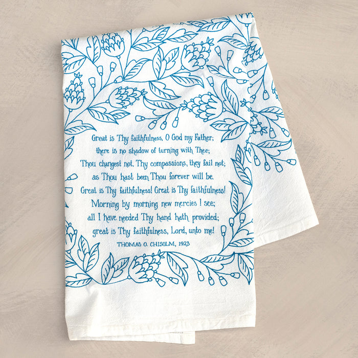 Great Is Thy Faithfulness tea towel is printed in a striking cerulean blue. The hand lettered text is surrounded by illustrated floral design, and the towel is shown folded against a khaki colored background.