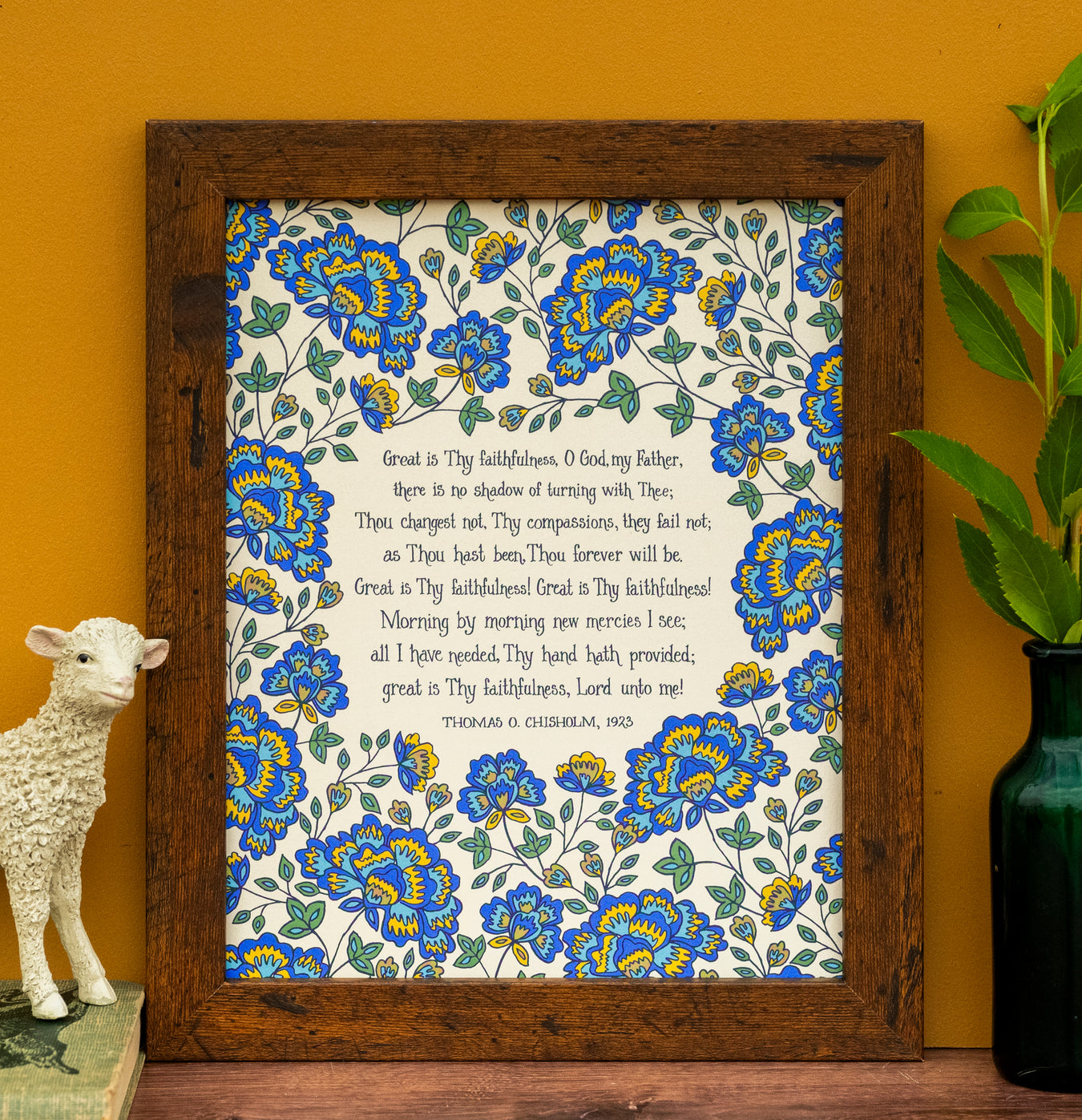 Great Is Thy Faithfulness hymn art print features the cherished hymn, surrounded by a bold blue and gold toned floral against a cream background; shown styled in a dark wood frame with a candle and a vase of flowers.