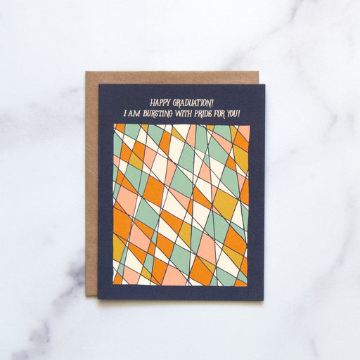 The graduation greeting card features abstract stained glass design that shines against a navy background, shown here against a white marble background.