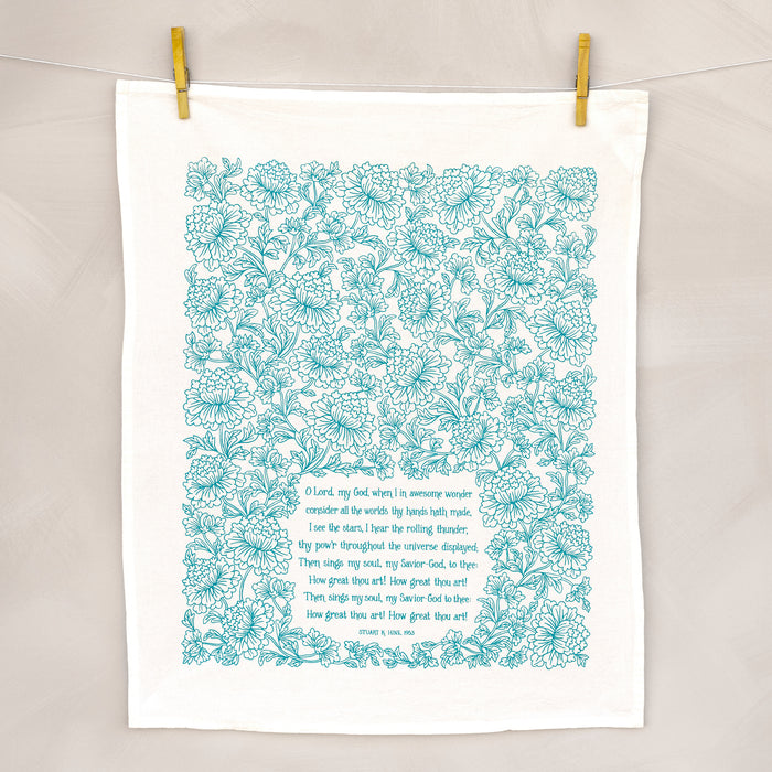 How great thou art tea towel in aqua blue unfolded and hanging with clothes pins