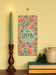 Celebrate 2025 with hymns both ancient and modern, bold floral patterns, and intricate hand-lettering, shown styled with a candle, ceramic jug, greens, and books, hung on an oatmeal toned wall.