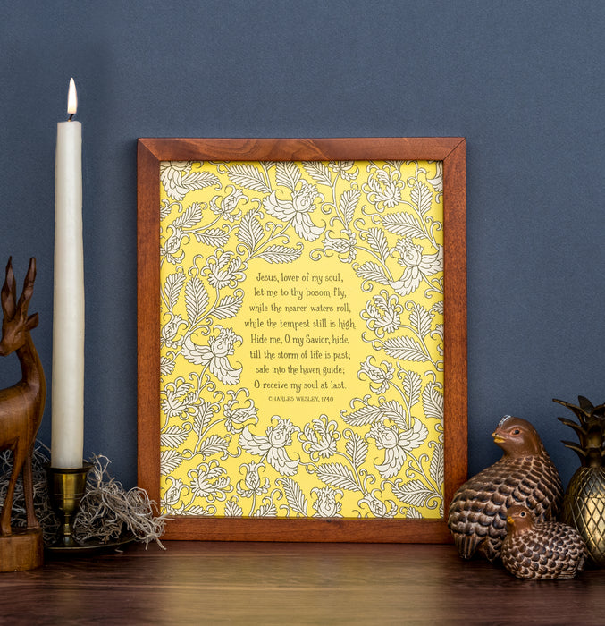 Jesus, Lover of My Soul hymn art print features a cream floral illustration against a yellow background, styled in a dark wood frame alongside a candle and ceramic figurines