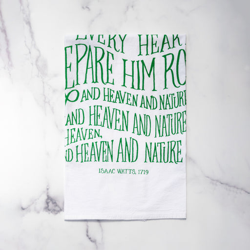 The "Joy to the World" hymn tea towel features printed, hand-lettered text in winter ivy on a 100% cotton tea towel. Made in the USA. Shown here folded against a marble background.