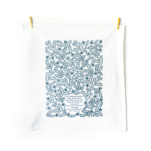 Leaning on the Everlasting Arms tea towel is printed in deep sea blue and features hand lettered hymn text surrounded by illustrated florals, pictured here unfolded and hanging with clothes pins against a white background.