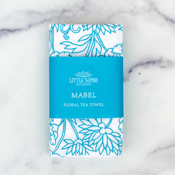 Little Things Studio presents floral tea towels — the Mabel floral tea towel features lively floral illustrations in vibrant turquoise, shown folded with a paper belly band for gift giving.